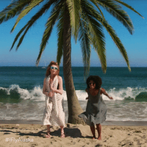 Two happy ladies jumping on the beach under a palm tree